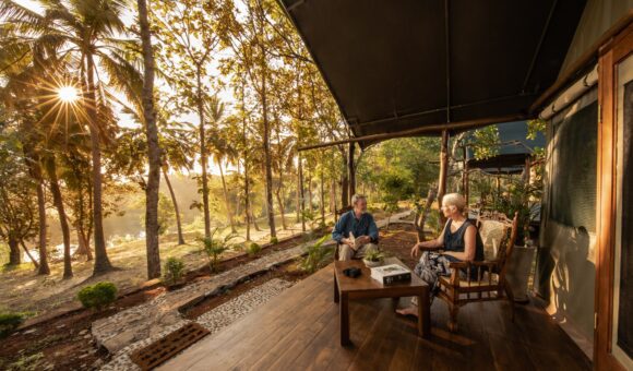 Two people sitting on a porch with trees in the background