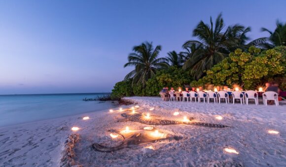 A group of people sitting around candles on the beach.