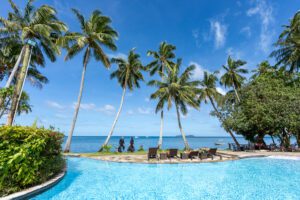 A pool with palm trees and people in the background.